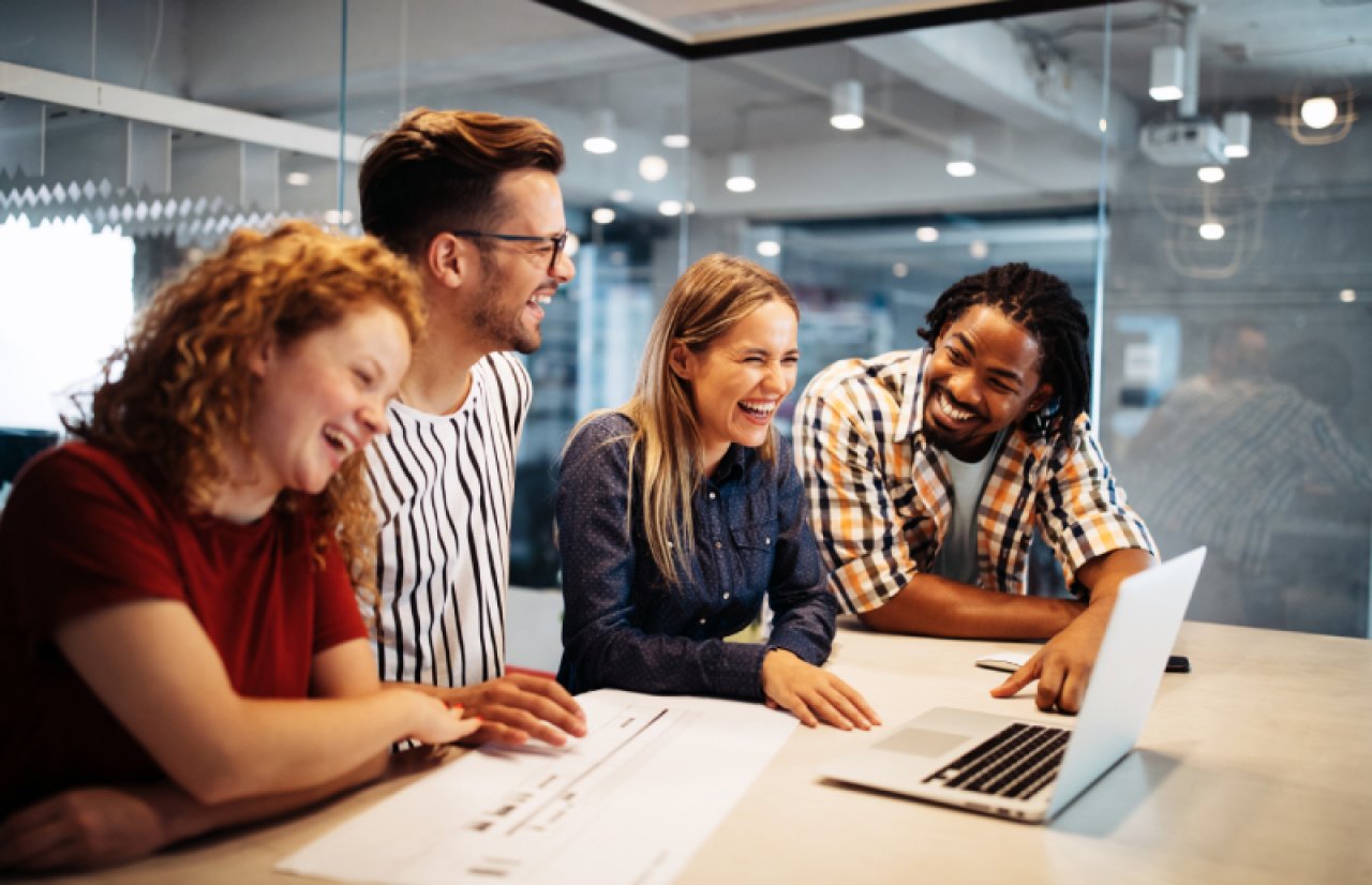 Group of young workers gathered around a laptop, laughing.