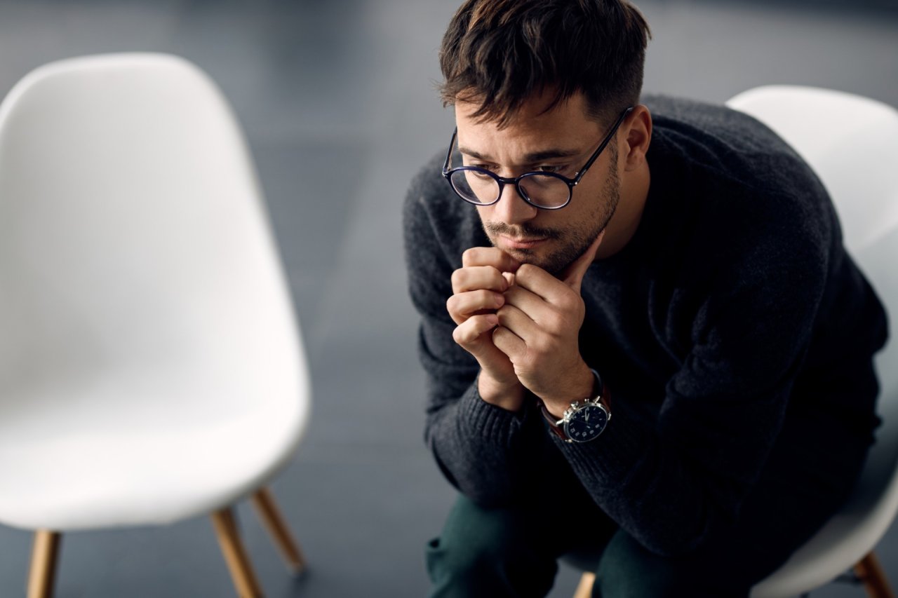 Man sat on chair, leaning forward looking worried.